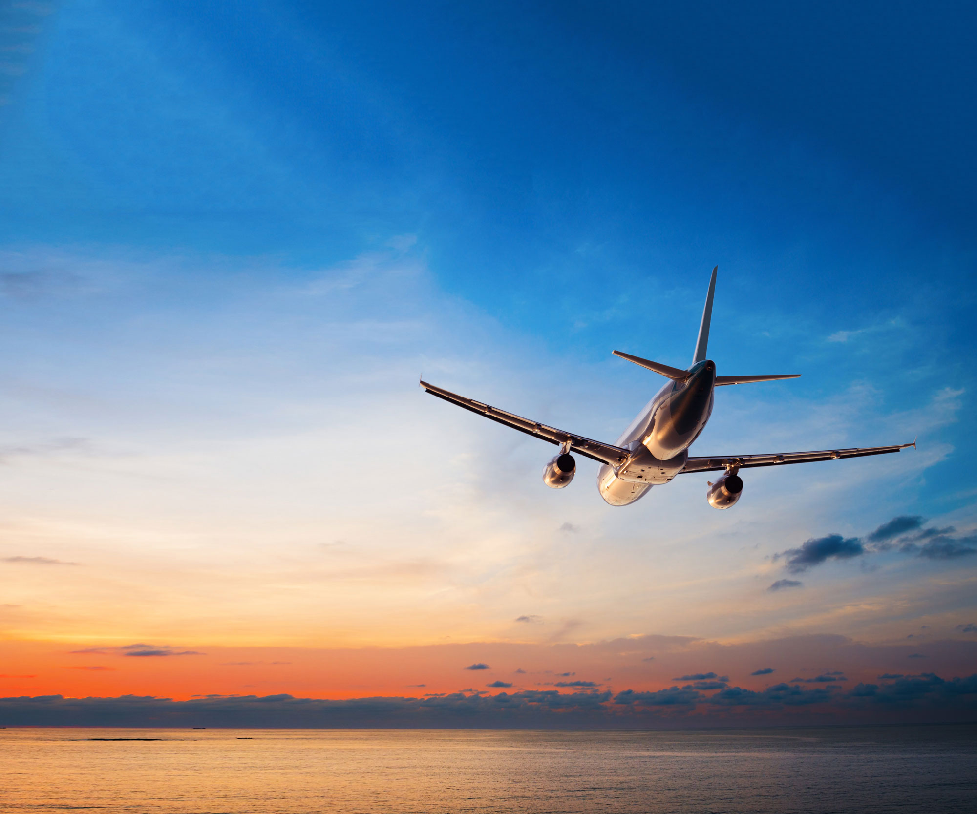plane flying in sunset sky over ocean